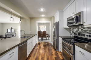 Kitchen with stainless steel appliances, decorative light fixtures, white cabinets, dark wood-style flooring, and a chandelier