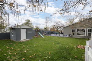 Fenced backyard featuring a playground, a storage unit, and a patio