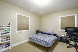 Bedroom with a textured ceiling, light carpet, and a desk