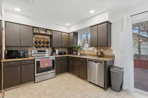 Kitchen with dark brown cabinets, stainless steel appliances, backsplash, light tile patterned floors, and light stone countertops