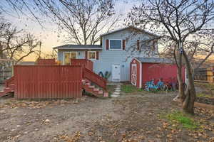 Back of house at dusk featuring a storage shed, a wooden deck, and stairs