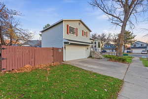 View of side of property featuring an attached garage, concrete driveway, and a gate