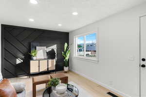 Living area with wood finished floors, recessed lighting, a textured ceiling, and an accent wall