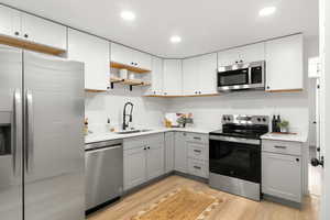 Kitchen with appliances with stainless steel finishes, open shelves, light wood-style flooring, gray cabinets, and recessed lighting