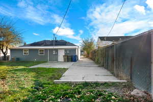 Back of house with roof mounted solar panels, a patio, and a fenced backyard