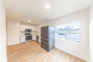 Kitchen featuring light countertops, white cabinetry, stainless steel appliances, light wood-style flooring, and recessed lighting