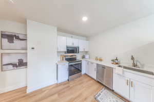 Kitchen featuring appliances with stainless steel finishes, white cabinets, light wood finished floors, light stone countertops, and recessed lighting