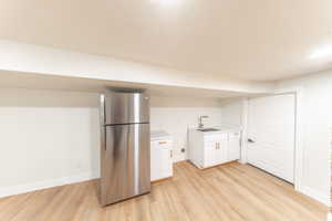 Kitchen with freestanding refrigerator, white cabinets, light countertops, and light wood-style floors