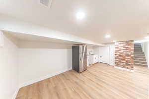 Finished basement with freestanding refrigerator and light wood-style floors
