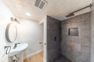Full bathroom with a tile shower, a textured ceiling, and wood finished floors