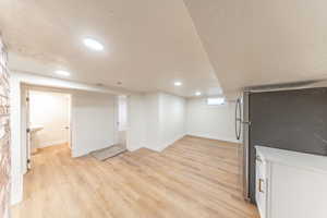 Basement featuring freestanding refrigerator, light wood finished floors, a textured ceiling, and recessed lighting