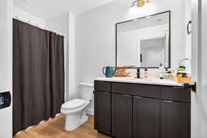 Full bath with a shower with curtain, light wood-type flooring, vanity, and a textured ceiling