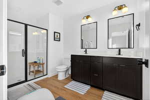 Full bathroom with double vanity, light wood-type flooring, and a shower stall