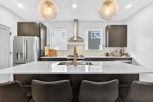 Kitchen with dark brown cabinets, a center island with sink, appliances with stainless steel finishes, wall chimney exhaust hood, and decorative backsplash