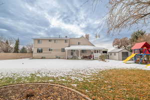 Snow covered house with a chimney, a playground, a patio area, and a shed