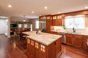 Kitchen featuring brown cabinetry, glass insert cabinets, stainless steel appliances, hanging light fixtures, and a kitchen island