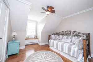 Bedroom featuring wood finished floors, a baseboard radiator, lofted ceiling, ceiling fan, and ornamental molding
