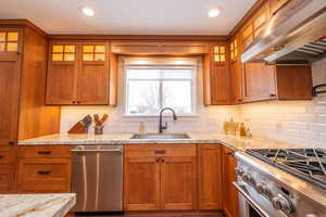 Kitchen featuring brown cabinets, glass insert cabinets, appliances with stainless steel finishes, range hood, and recessed lighting