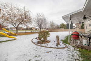 Snowy yard with a playground, a fenced backyard, a ceiling fan, and a residential view