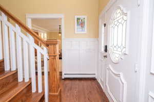 Foyer with a wainscoted wall, a decorative wall, baseboard heating, stairway, and dark wood-style floors