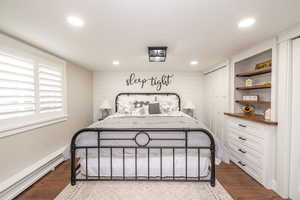 Bedroom with dark wood-style flooring, a closet, wooden walls, baseboard heating, and recessed lighting