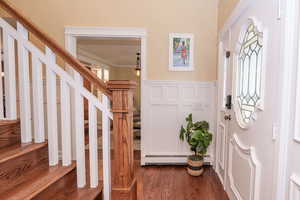Entryway with a decorative wall, a wainscoted wall, dark wood-type flooring, a baseboard radiator, and stairway