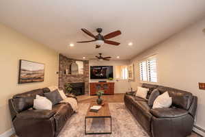 Living room with a fireplace, a baseboard heating unit, ceiling fan, and light carpet