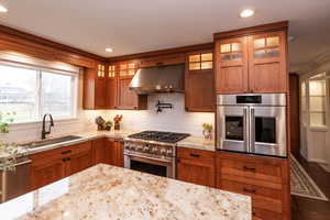 Kitchen featuring brown cabinetry, appliances with stainless steel finishes, glass insert cabinets, under cabinet range hood, and recessed lighting