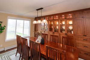 Dining space with a baseboard heating unit, ornamental molding, and wood finished floors