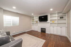 Living area featuring a baseboard radiator, a fireplace, dark wood-style floors, built in features, and recessed lighting