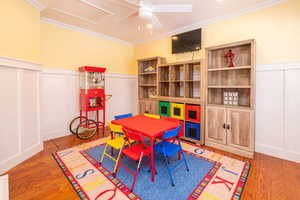 Recreation room featuring a decorative wall, wainscoting, crown molding, light wood-style floors, and ceiling fan
