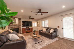 Living area with a fireplace, light colored carpet, a baseboard heating unit, and a ceiling fan