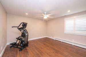 2nd Bedroom downstairs that is currently used as a workout room with baseboard heating, dark wood finished floors, a ceiling fan, and recessed lighting