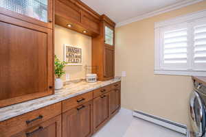 Washroom featuring a baseboard radiator, washer / dryer, crown molding, and cabinet space