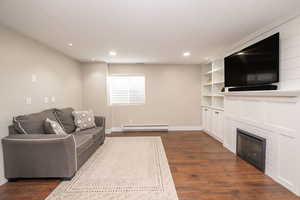 Living room featuring a glass covered fireplace, dark wood finished floors, recessed lighting, a baseboard heating unit, and built in features