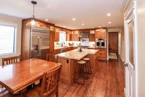 Kitchen with brown cabinets, appliances with stainless steel finishes, decorative light fixtures, a kitchen island, and crown molding