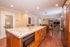 Kitchen featuring brown cabinetry, dark wood finished floors, a kitchen island, built in appliances, and ornamental molding