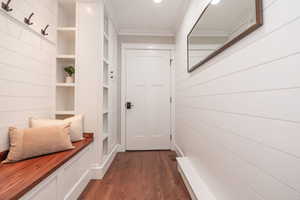 Mudroom with built in features, crown molding, and dark wood-type flooring
