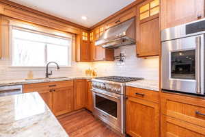 Kitchen featuring stainless steel appliances, wall oven with french doors (perfect height!), ventilation hood, glass insert cabinets, brown cabinetry, and recessed lighting