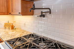 Kitchen view of pot filler, black gas stovetop, light stone countertops, and decorative backsplash