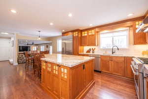 Kitchen featuring brown cabinetry, glass insert cabinets, high end appliances, a center island, and crown molding