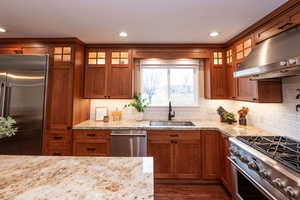 Kitchen featuring glass insert cabinets, brown cabinetry, high end appliances, under cabinet range hood, and recessed lighting