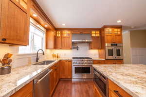Kitchen featuring brown cabinets, appliances with stainless steel finishes, glass insert cabinets, and recessed lighting