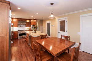Dining room with dark wood finished floors, ornamental molding, recessed lighting, and beverage cooler
