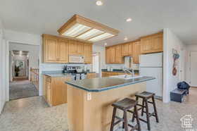 Kitchen with a breakfast bar, light brown cabinets, white appliances, a center island with sink, and recessed lighting
