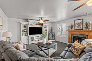 Living area with a ceiling fan, a fireplace, dark carpet, and a textured ceiling