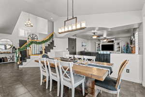 Dining space with stairway, a chandelier, high vaulted ceiling, ceiling fan, and dark tile patterned flooring