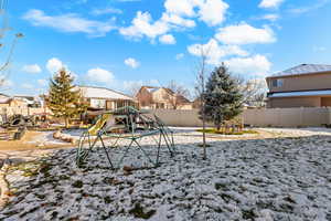 Snow covered playground featuring a residential view, a fenced backyard, and a playground