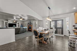 Dining room featuring vaulted ceiling, a lit fireplace, ceiling fan, arched walkways, and dark colored carpet