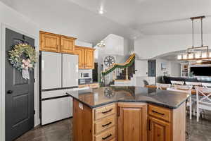 Kitchen featuring freestanding refrigerator, dark stone counters, a center island, vaulted ceiling, and open floor plan